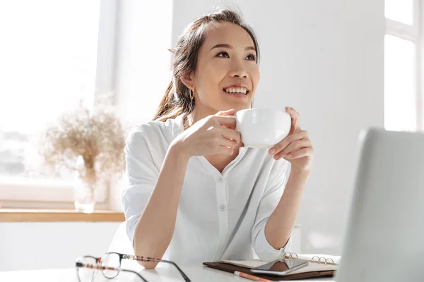 Pensive усміхнений азіатський бізнес жінка п'є каву і дивиться геть — стокове фото