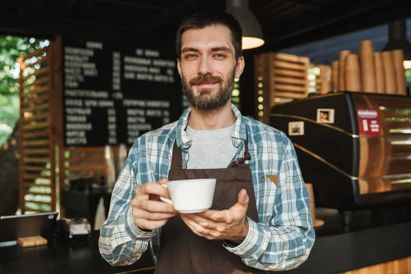 Retrato del barista sonriente sosteniendo una taza de café mientras trabaja —  Fotos de Stock