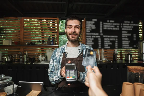 Retrato de homem barista afável levando cartão de crédito do cliente — Fotografia de Stock