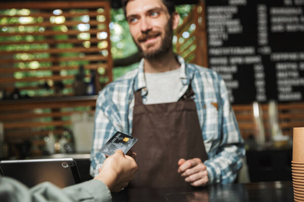 Portrait of young barista man taking credit card from customer w