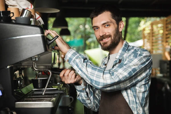 Imagen del hombre barista sonriente haciendo café mientras trabaja en la cafetería —  Fotos de Stock