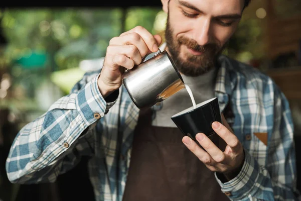 Imagen del alegre camarero haciendo café mientras trabajaba en la cafetería —  Fotos de Stock