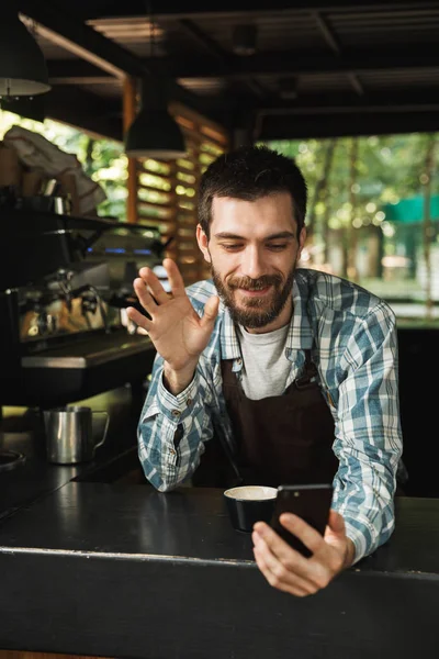 Foto des kaukasischen Barista-Typen, der lächelt, während er das Smartphone benutzt — Stockfoto