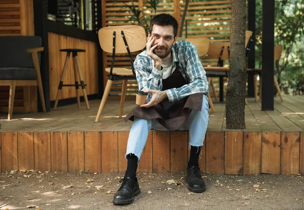 Foto di gioioso cameriere seduto sul pavimento in legno mentre lavorava — Foto Stock