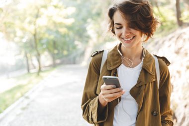 Genç ve güzel bir kadın güzel bir bahar gününde parkta cep telefonu kullanarak yürüyor..