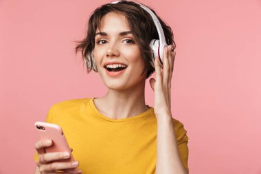 Mutlu genç güzel kadın cep telefonu kullanarak kulaklık ile müzik dinleme pembe duvar arka plan üzerinde izole poz.