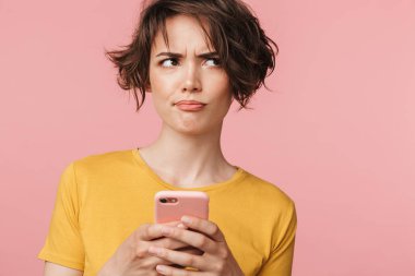 Şaşkın genç güzel kadın cep telefonu kullanarak pembe duvar arka plan üzerinde izole poz.