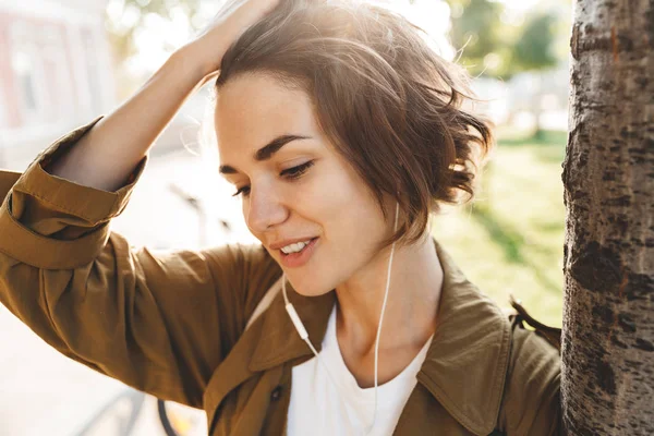 Веселая красивая женщина гуляет по парку в красивый весенний день, слушая музыку с наушниками . — стоковое фото