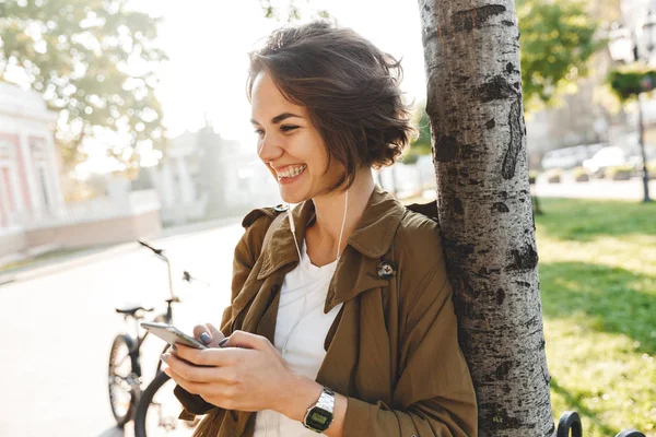 Jovem mulher bonita andando ao ar livre no parque no belo dia de primavera usando telefone móvel . — Fotografia de Stock