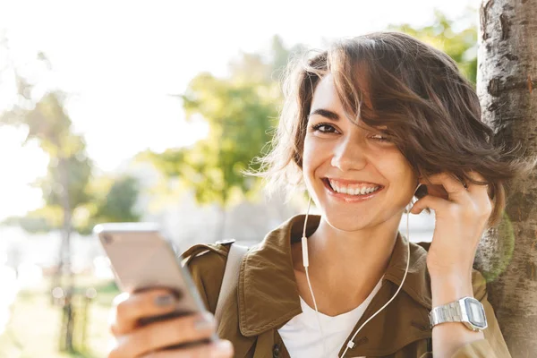 Mujer bonita joven caminando al aire libre en el parque en hermoso día de primavera utilizando el teléfono móvil . — Foto de Stock