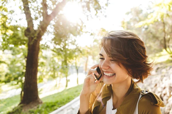 Bonito jovem mulher incrível andando ao ar livre no parque em belo dia de primavera falando por telefone celular . — Fotografia de Stock