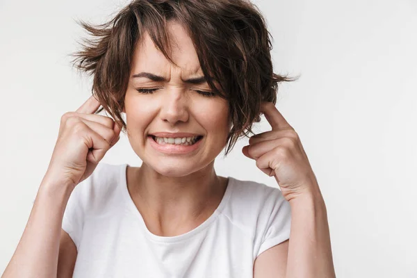 Ziemlich unzufrieden gestresste Frau posiert isoliert über weiße Wand Hintergrund bedecken Ohren wegen der lauten. — Stockfoto