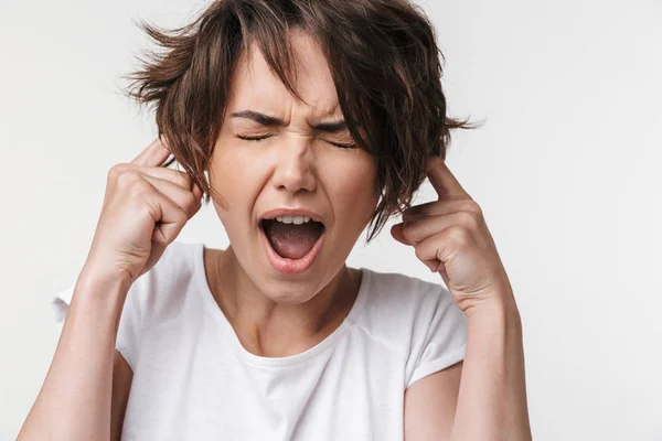 Ganska missnöjd stressad kvinna poserar isolerade över vit vägg bakgrund som täcker öron på grund av högt. — Stockfoto