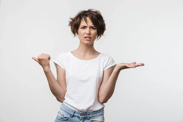 Young pretty displeased shocked woman posing isolated over white wall background pointing to copyspace. — ストック写真