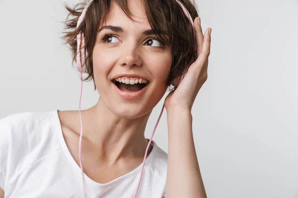 Ganska upphetsad lycklig kvinna poserar isolerade över vit vägg bakgrund lyssnar musik med hörlurar. — Stockfoto