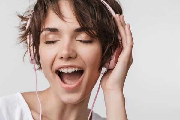 Ganska upphetsad lycklig kvinna poserar isolerade över vit vägg bakgrund lyssnar musik med hörlurar. — Stockfoto