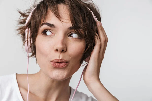 Ganska upphetsad lycklig kvinna poserar isolerade över vit vägg bakgrund lyssnar musik med hörlurar. — Stockfoto