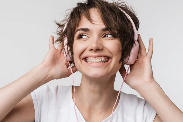 Ziemlich aufgeregt glücklich Frau posiert isoliert über weiße Wand Hintergrund Musik hören mit Kopfhörern. — Stockfoto