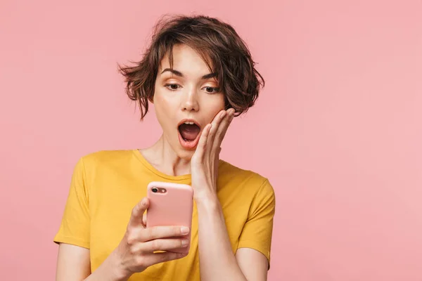 Joven mujer hermosa impactada posando aislada sobre fondo de pared rosa usando teléfono móvil . — Foto de Stock