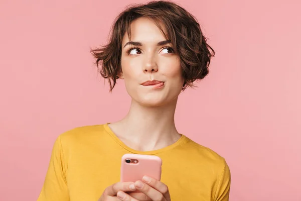 Pensando soñando joven hermosa mujer posando aislado sobre fondo de pared rosa utilizando el teléfono móvil. —  Fotos de Stock