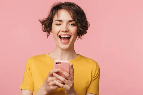 Gelukkig jonge mooie vrouw poseren geïsoleerd over roze muur achtergrond met behulp van mobiele telefoon. — Stockfoto