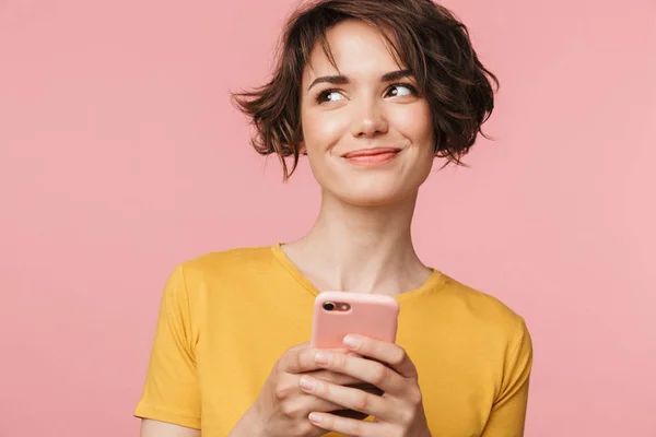 Думаю, мечтая молодая красивая женщина позирует изолированы на розовом фоне стены с помощью мобильного телефона. — стоковое фото