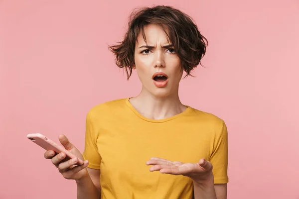 Joven mujer hermosa impactada posando aislada sobre fondo de pared rosa usando teléfono móvil . — Foto de Stock