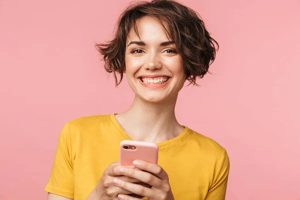 Счастливая молодая красивая женщина позирует изолированы на розовом фоне стены с помощью мобильного телефона . — стоковое фото