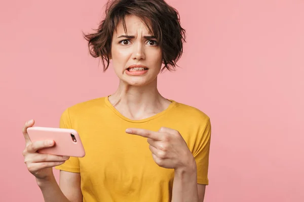 Confundido sorprendido joven hermosa mujer posando aislado sobre la pared rosa de fondo jugar juegos por teléfono móvil . — Foto de Stock