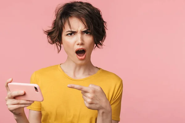 混乱したショックを受けた若い美しい女性は、携帯電話でピンクの壁の背景の上に孤立したポーズ. — ストック写真