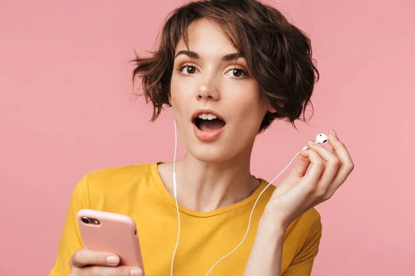 Concentrado jovem bela mulher posando isolado sobre fundo de parede rosa ouvir música com fones de ouvido usando telefone celular tentar ouvi-lo . — Fotografia de Stock