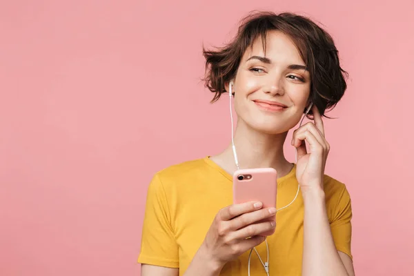 Щаслива молода красива жінка позує ізольовано на рожевому фоні стіни, слухаючи музику з навушниками за допомогою мобільного телефону . — стокове фото