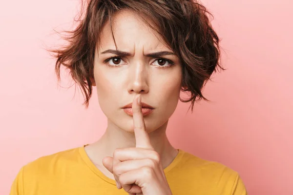 Ernstige mooie vrouw poseren geïsoleerd over roze muur achtergrond toont stilte gebaar. — Stockfoto