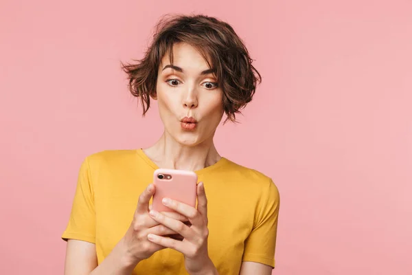 Joven mujer hermosa impactada posando aislada sobre fondo de pared rosa usando teléfono móvil . —  Fotos de Stock