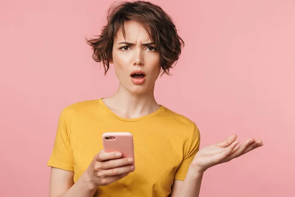 Schockierte junge schöne Frau posiert isoliert über rosa Wand Hintergrund mit Handy. — Stockfoto