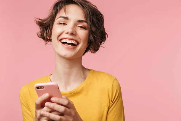 Щаслива молода красива жінка позує ізольовано на рожевому фоні стіни за допомогою мобільного телефону . — стокове фото