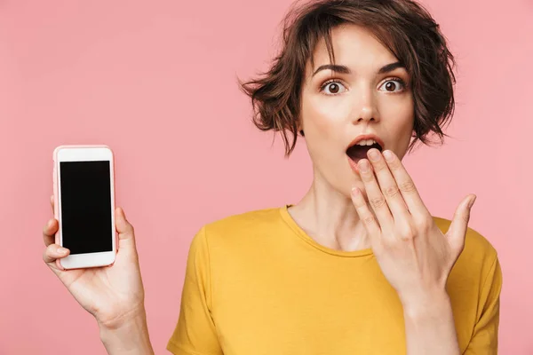 Joven mujer hermosa impactada posando aislada sobre fondo de pared rosa usando teléfono móvil . — Foto de Stock