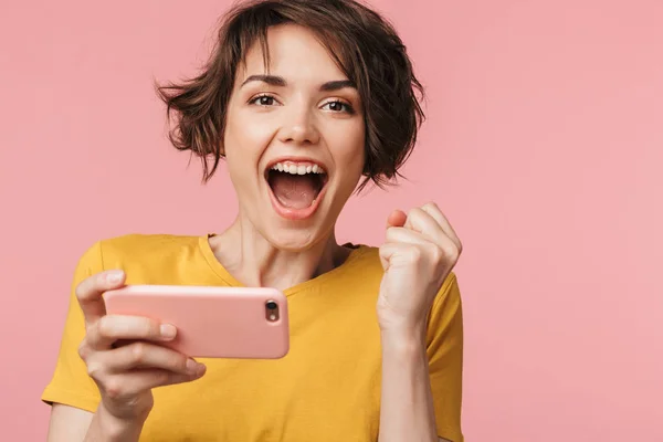 Joyeux jeune belle femme posant isolé sur fond de mur rose jouer à des jeux par téléphone mobile . — Photo