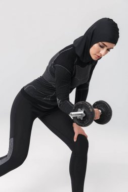 Kadın fitness müslümanı, beyaz arka planda yalnız poz veriyor. Dambılla egzersiz yapıyor..