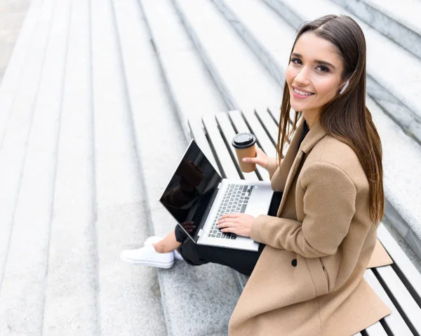 Όμορφη νεαρή γυναίκα φορώντας φθινόπωρο παλτό χρησιμοποιώντας φορητό υπολογιστή — Φωτογραφία Αρχείου