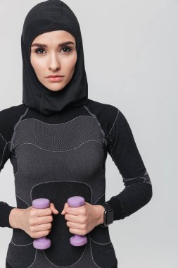 Genç kadın fitness müslümanı, beyaz duvar arkasına izole edilmiş halterlerle egzersiz yapıyor..