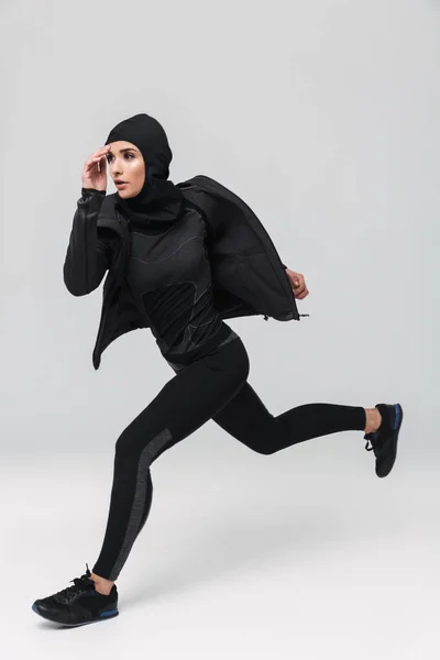 Fitness muzułmańska kobieta stwarzające bieganie skoki izolowane na białym tle ściany. — Zdjęcie stockowe