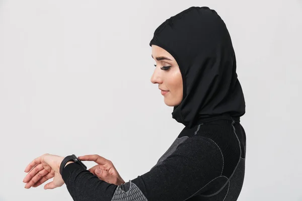 Młoda kobieta fitness muzułmanin za pomocą zegara odizolowane na białym tle ściany. — Zdjęcie stockowe