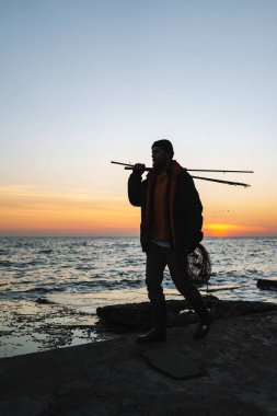 Ceket giyen adam balıkçı silueti, çubuk tutan