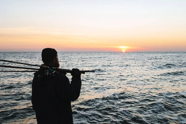 Silhouette of man fisherman wearing coat, holding rod