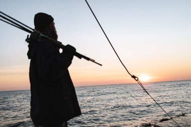 Ceket giyen adam balıkçı silueti, çubuk tutan