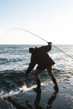 Ceket giyen adam balıkçı silueti, çubuk tutan