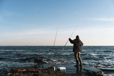 Yakışıklı genç adam balıkçı sahilde ceket ve şapka giyiyor.