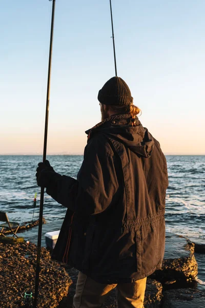 Человек рыбак в пальто стоит с удочкой — стоковое фото