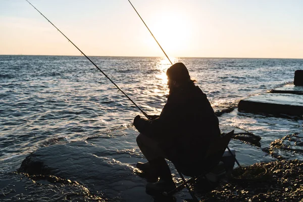 Silhouette of man fisherman wearing coat, holding rod